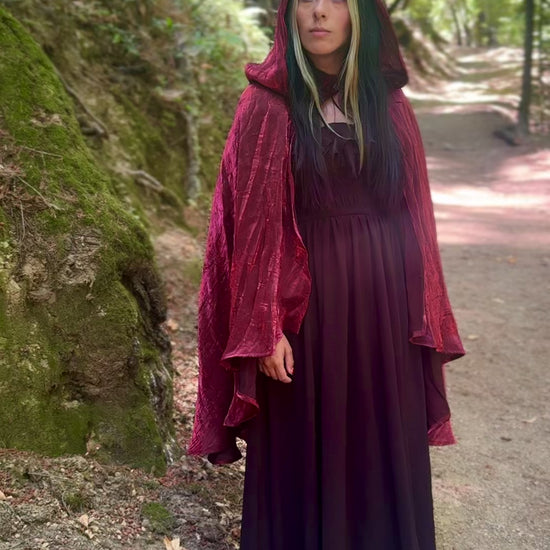 Person wearing a red hooded cape in a forest setting.