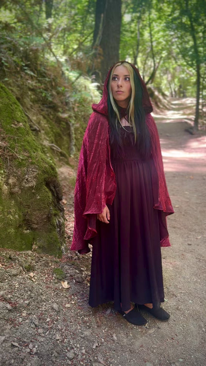 Person wearing a red hooded cape in a forest setting.