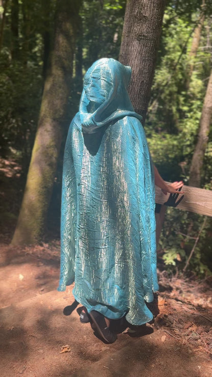 Person wearing a sky blue cloak in a forest