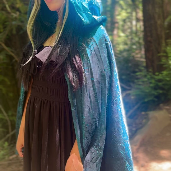 Person wearing a blue cape, standing in a forest