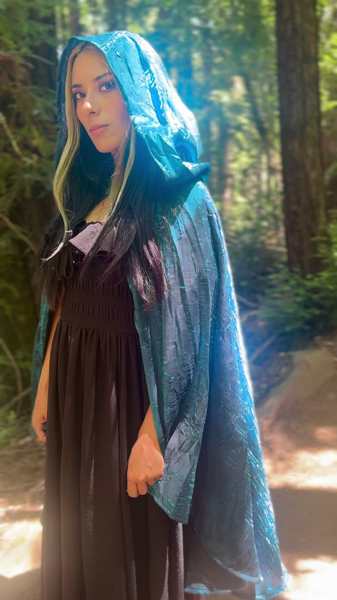 Person wearing a blue cape, standing in a forest