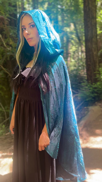 Person wearing a blue cape, standing in a forest