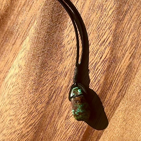 Turquoise stone pendant on a leather cord against a wooden background, spinning.