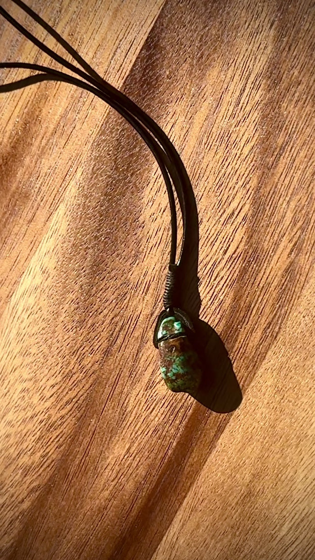 Turquoise stone pendant on a leather cord against a wooden background, spinning.