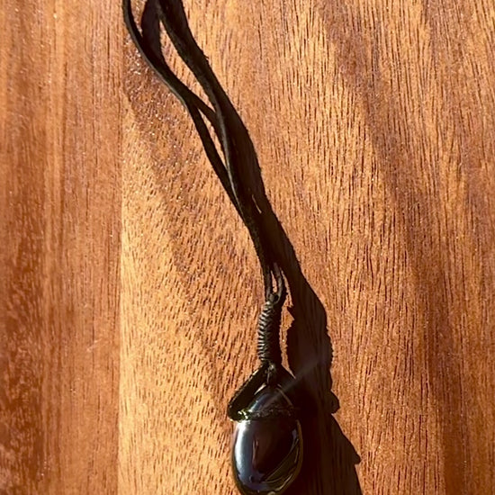 Magnetic Black Hematite stone pendant wrapped in a black leather cord against a wooden surface, spinning.