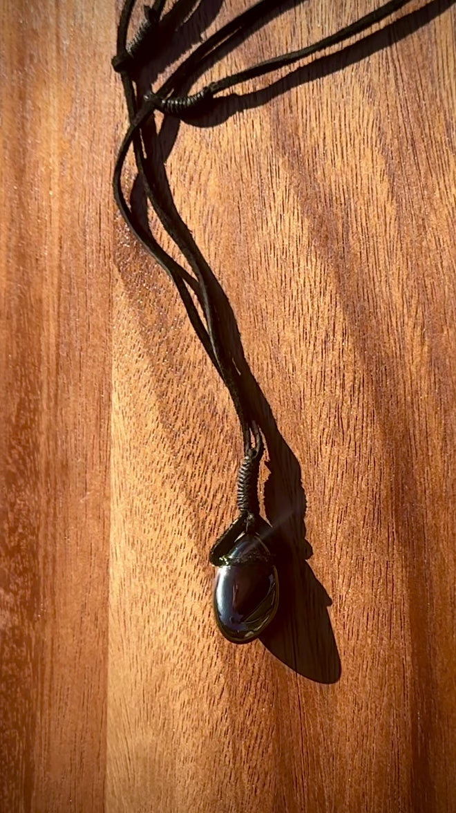 Magnetic Black Hematite stone pendant wrapped in a black leather cord against a wooden surface, spinning.