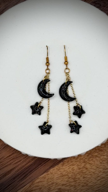 Pair of rainbow glitter black crescent moon and star earrings with gold hooks on a white background