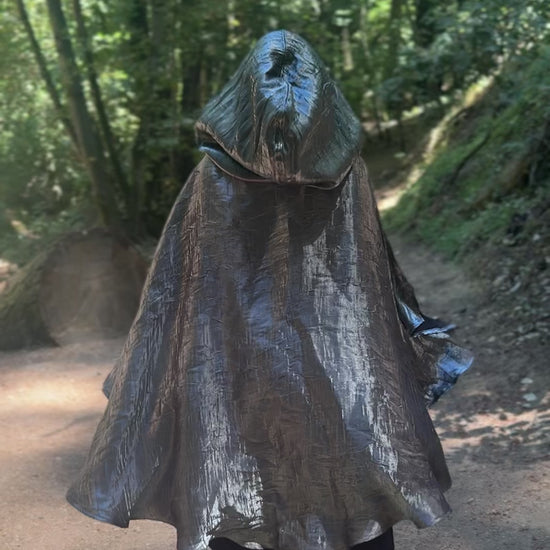 Person wearing a silver hooded cloak in a forest setting, walking