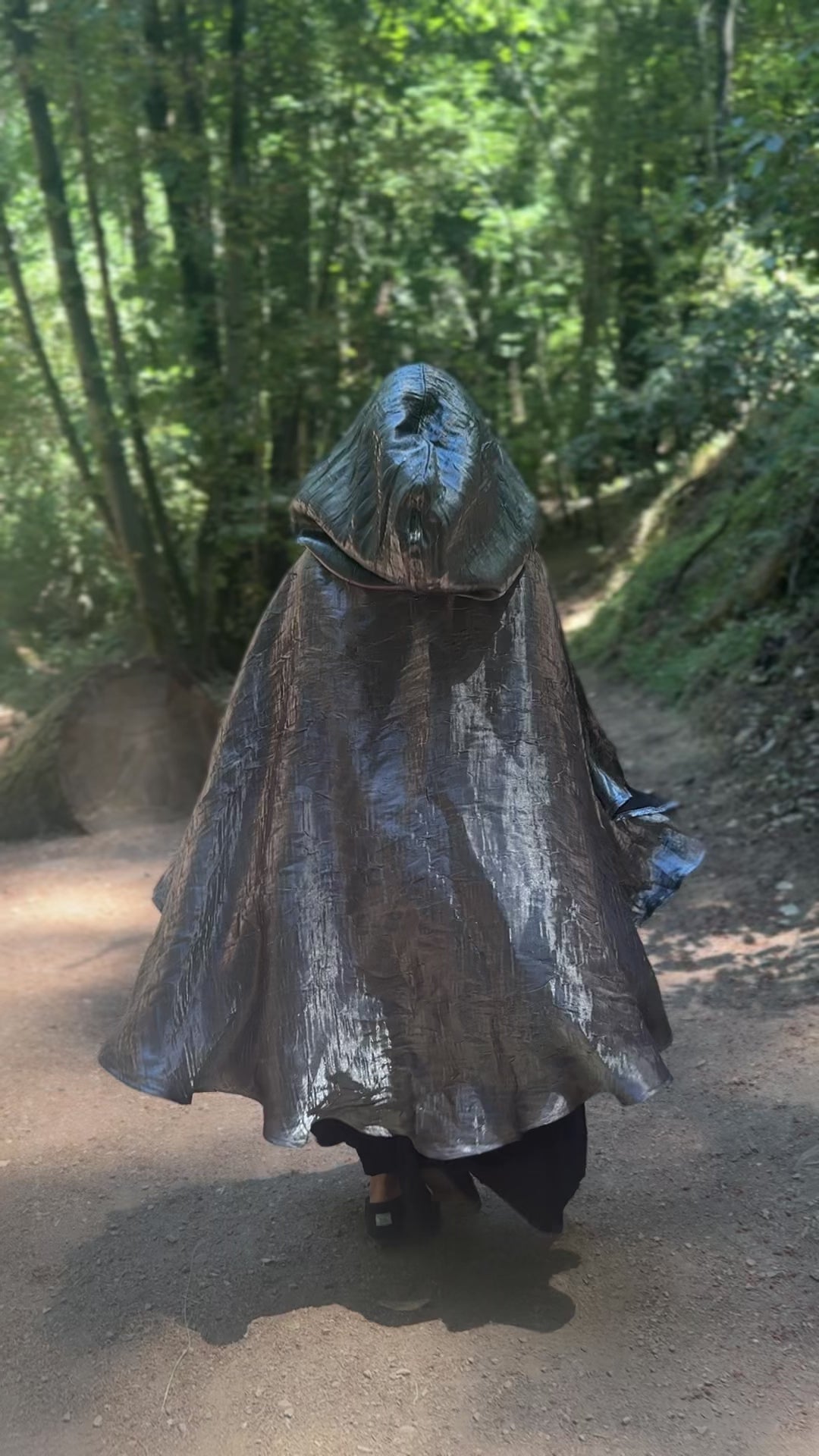 Person wearing a silver hooded cloak in a forest setting, walking