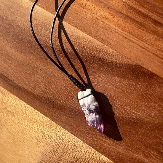 Large rough cut white and purple Amethyst crystal necklace on a wooden surface, spinning.