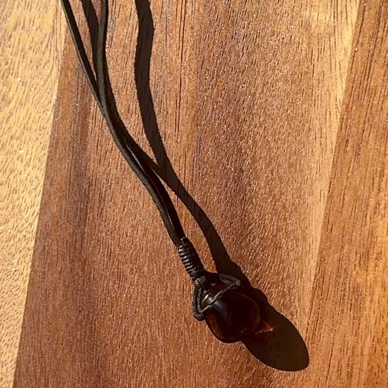 Smoky dark quartz stone pendant wrapped in a black leather cord against a wooden surface, spinning.