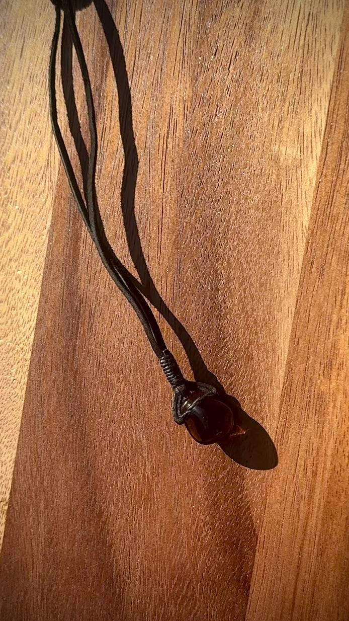 Smoky dark quartz stone pendant wrapped in a black leather cord against a wooden surface, spinning.