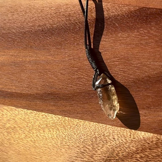 Garden Quartz stone pendant on a leather cord against a wooden background, spinning.