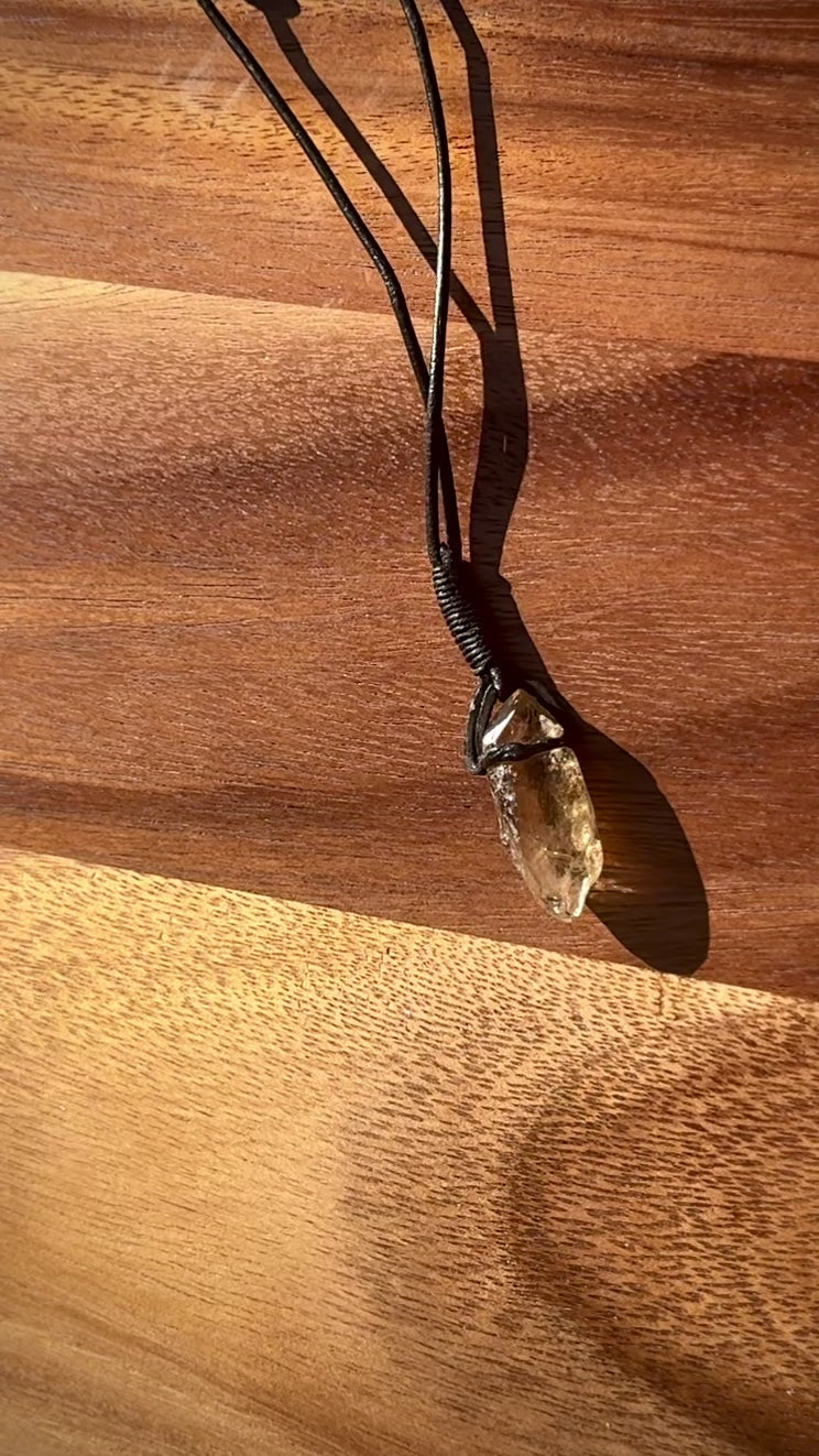 Garden Quartz stone pendant on a leather cord against a wooden background, spinning.