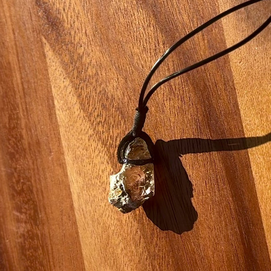 Large chunk of Garden Quartz stone pendant on a leather cord against a wooden background, spinning.