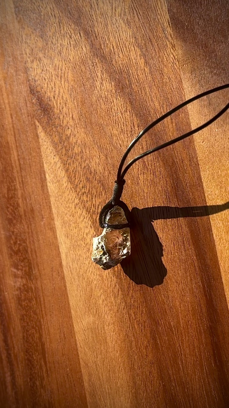 Large chunk of Garden Quartz stone pendant on a leather cord against a wooden background, spinning.