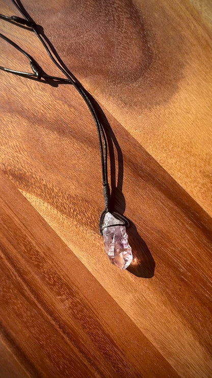 Amethyst stone pendant with inclusions on a leather cord against a wooden background, spinning.