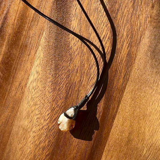 citrine crystal with leather necklace band on a wooden table, spinning