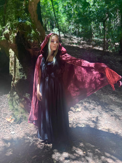 Person wearing a red hooded cloak in a forest setting