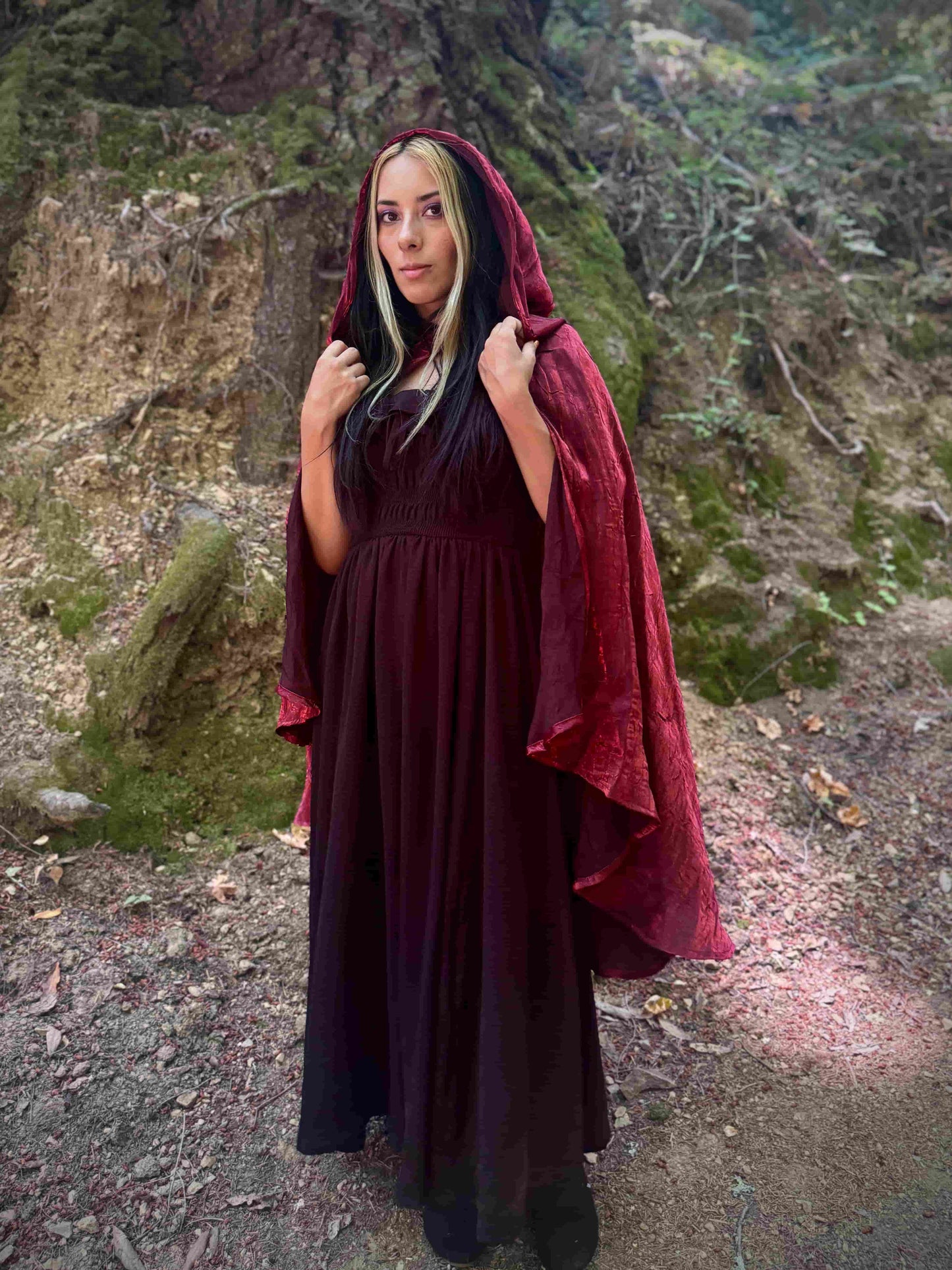 Person wearing a dark red hooded cloak in a natural setting