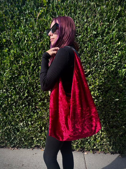 Person holding a red velvet slouchy shoulder bag against a green hedge background