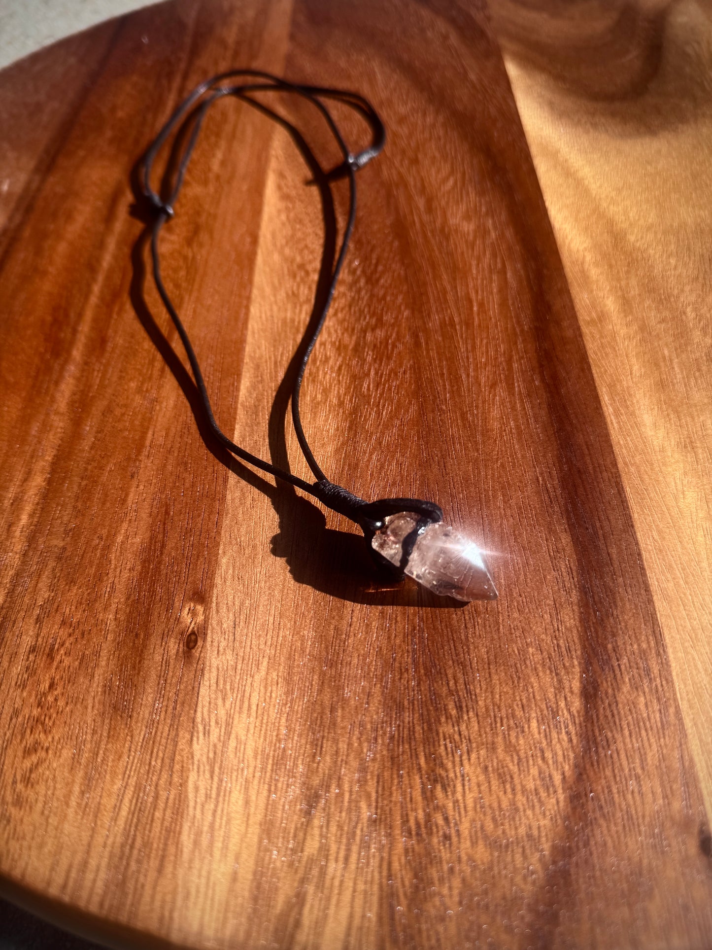 Crystal pendant on a black cord on a wooden surface