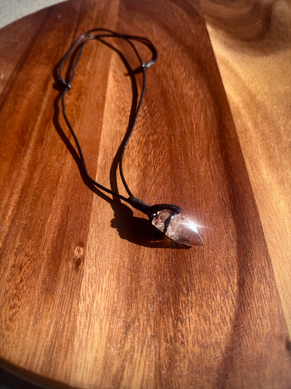 Crystal pendant on a black cord on a wooden surface