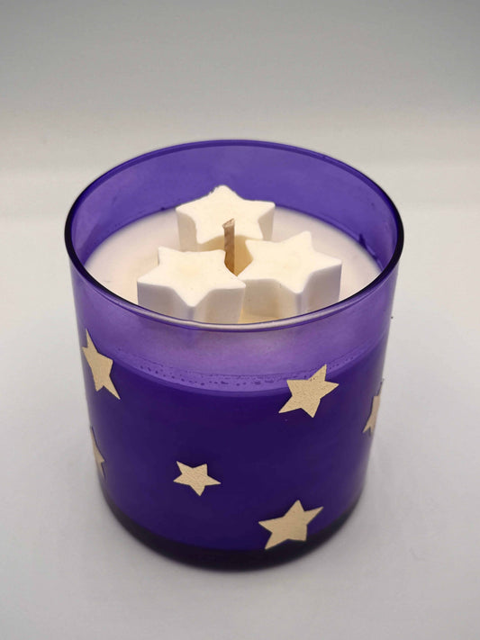 Candle in a purple container with star patterns on a gray background